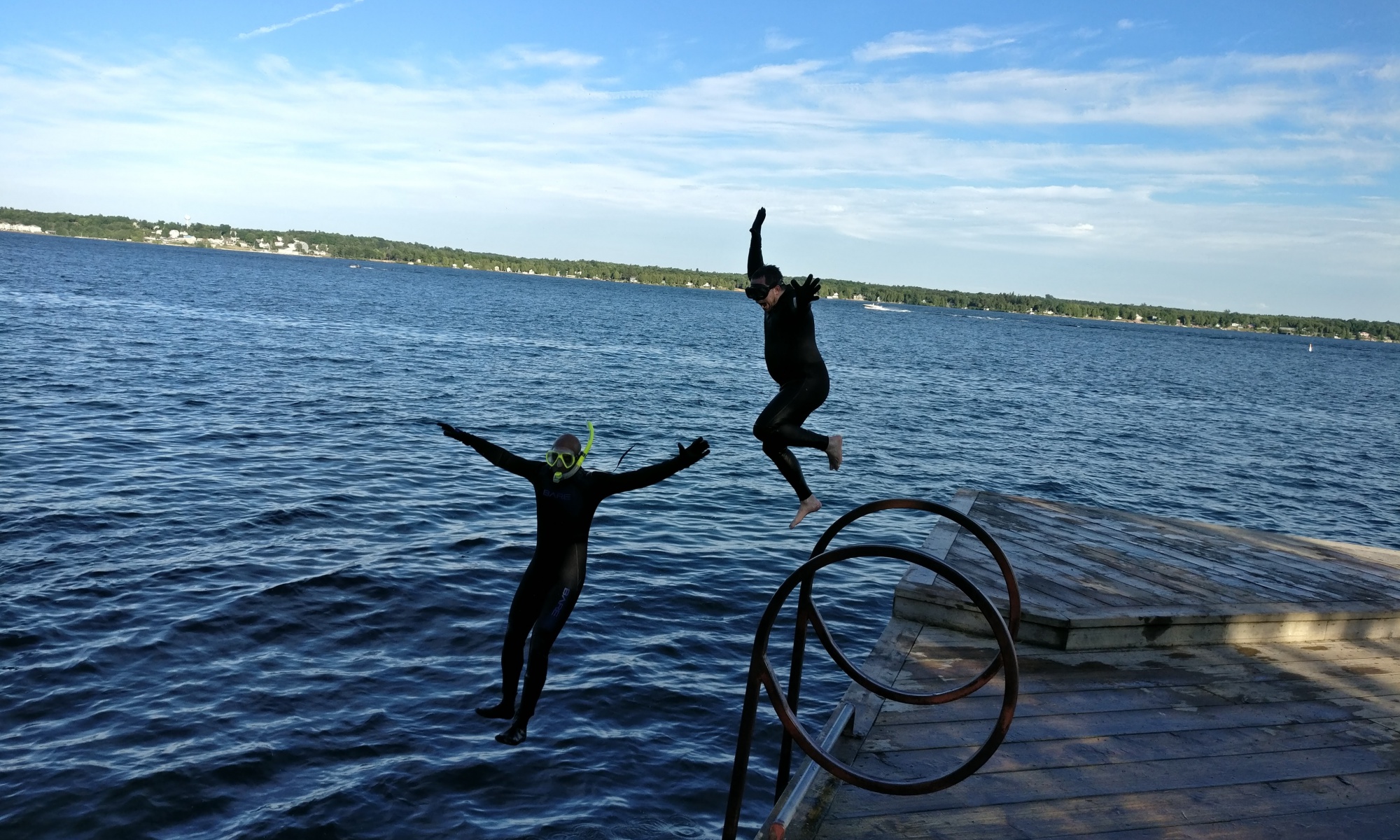 HHUC wetsuited snorkellers joyously jumping off a dock into the lake