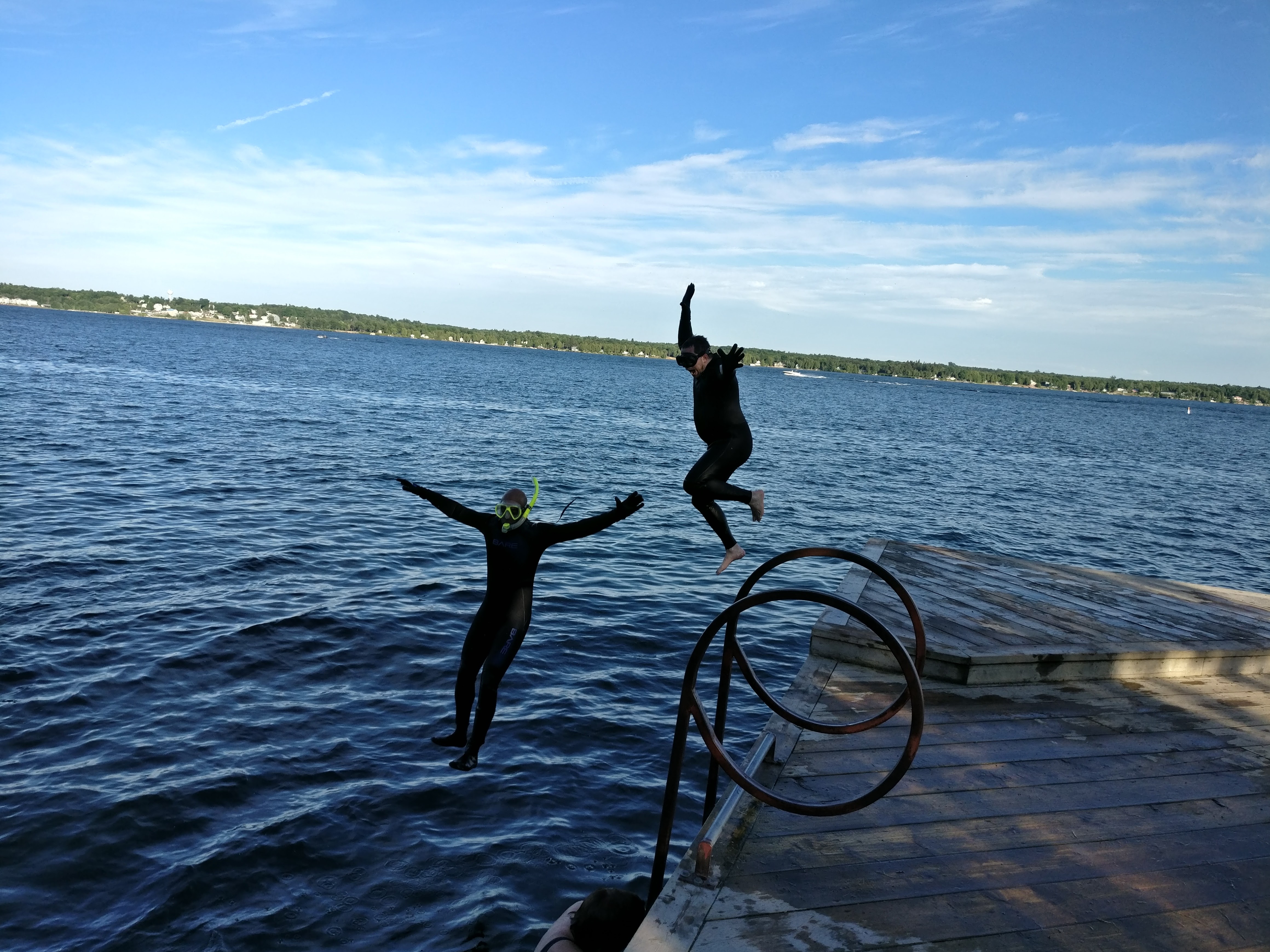 HHUC wetsuited snorkellers joyously jumping off a dock into the lake